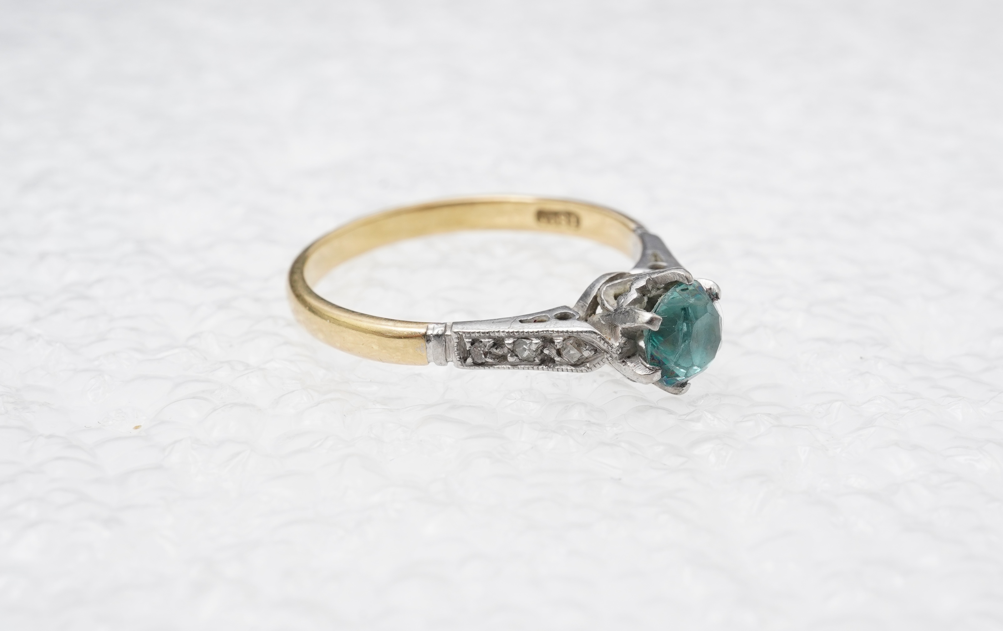 A zircon and diamond ring, mid 20th century, claw-set with a brilliant-cut blue zircon measuring approximately 5mm diameter, to shoulders set with rose-cut diamonds, mounted in gold, size N, stamped 18CT, gross weight ap